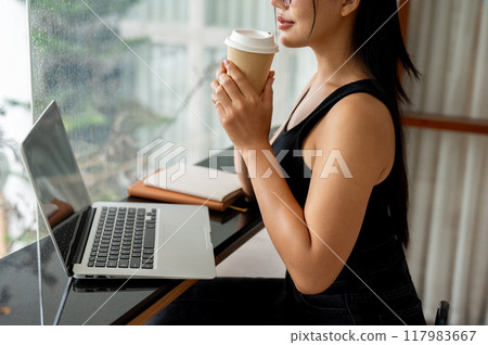 A woman enjoying coffee while working remotely from a modern, minimalist coffee shop. A woman enjoying coffee while working remotely from a modern, minimalist coffee shop. 117983667