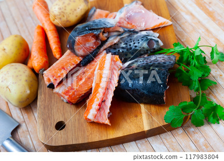 There are salmon trimmings on cutting board - head, spine, tail with potatoes, carrots, parsley There are salmon trimmings on cutting board - head, spine, tail with potatoes, carrots, parsley 117983804