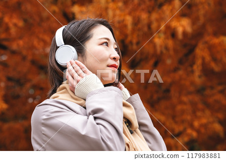A young woman immersed in music among autumn leaves 117983881
