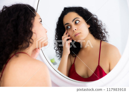 Young woman checking face skin in mirror Young woman checking face skin in mirror 117983918