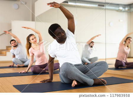 Man practising lotus pose with group in gym 117983938