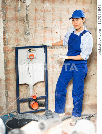 Portrait of female plumber in blue overall next to sewerage system being installed 117983948