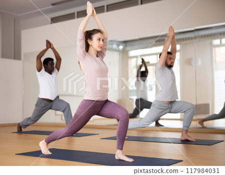 People exercising warrior one asana in gym 117984031
