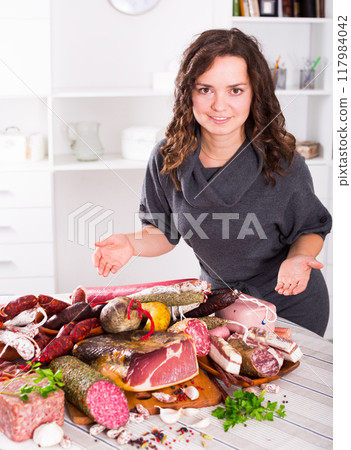 Girl shows sausages and smoked products Girl shows sausages and smoked products 117984042
