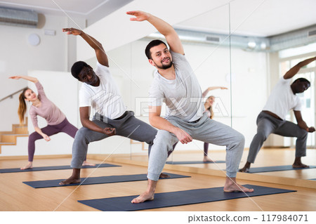 Young man stretching during Hatha yoga with group in studio 117984071