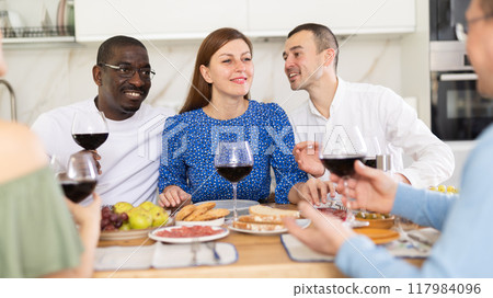 Cheerful adult friends dining and chatting in home kitchen 117984096