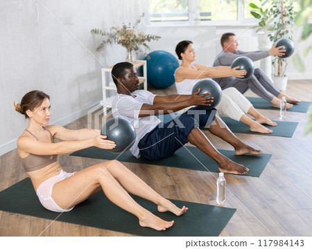 Positive women and men posing with soft ball pilates at group class in yoga studio 117984143