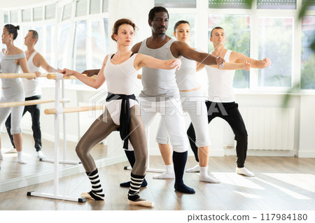 Graceful women and sports men practice at ballet standing at barre in choreography class 117984180