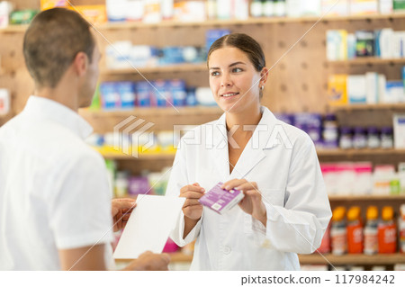 Female pharmacist consulting young guy about medicament according to recipe Female pharmacist consulting young guy about medicament according to recipe 117984242