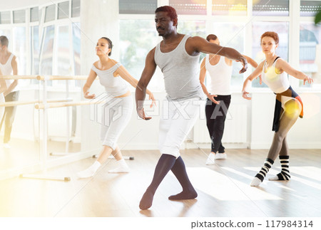 Group of men and women of different nationalities rehearsing ballet movements in studio 117984314