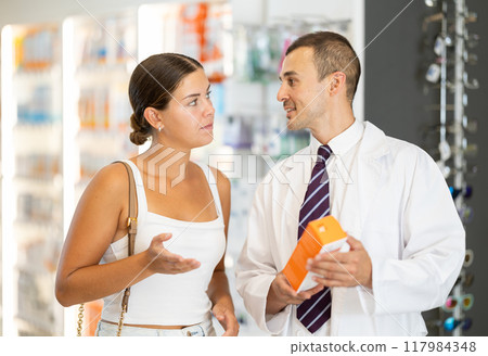 Male pharmacist consulting young girl about medicament in box 117984348