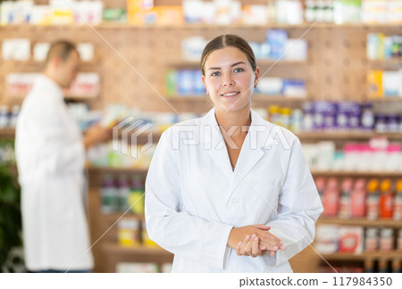 Young female pharmacist welcoming clients in chemist's shop 117984350