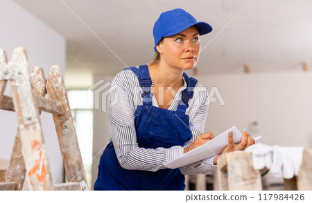Female foreman in blue workwear making task list in building under construction Female foreman in blue workwear making task list in building under construction 117984426