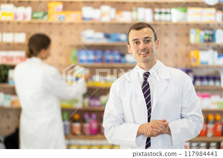 At pharmacy, man apothecary waiting for customers, invite with gesture go to department of cosmetic At pharmacy, man apothecary waiting for customers, invite with gesture go to department of cosmetic 117984441