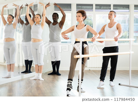 Ballet rehearsal in dance studio - men and women stand in second position near ballet barre 117984450