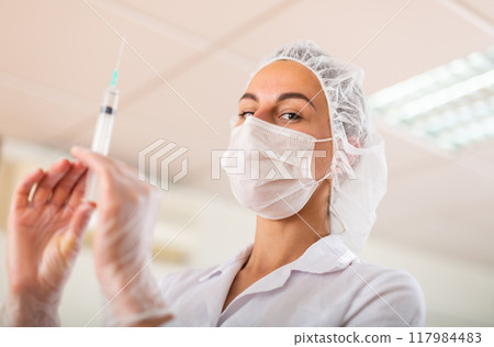 Nurse prepares a syringe for injection 117984483