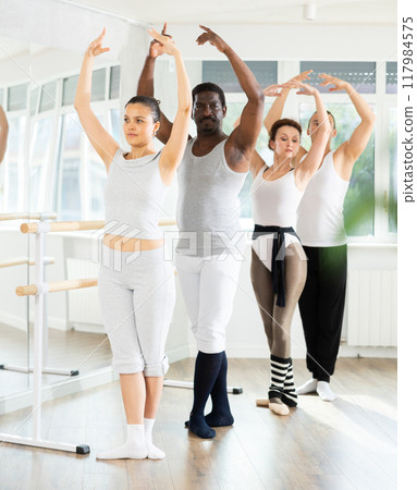 Ballet troupe stand in fifth position near ballet barre during group training in dance studio Ballet troupe stand in fifth position near ballet barre during group training in dance studio 117984575