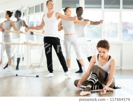 Female dancer adjusting point shoes on floor in ballet studio 117984579