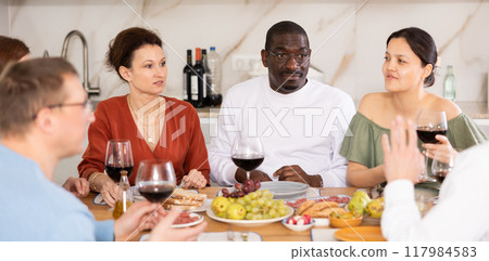 Happy adult friends at the festive table discussing news and drinking red wine Happy adult friends at the festive table discussing news and drinking red wine 117984583