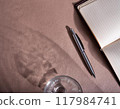 Shadow of a glass of water, notebook and pen 117984741