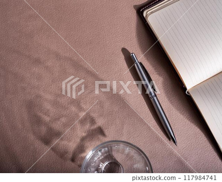 Shadow of a glass of water, notebook and pen 117984741
