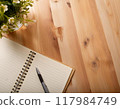 An open spiral notebook on a wooden table with a vase 117984749