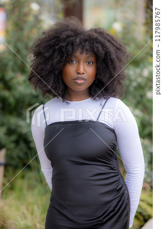 A stylish, confident young woman with chic curly hair in an elegant outdoor setting A stylish, confident young woman with chic curly hair in an elegant outdoor setting 117985767