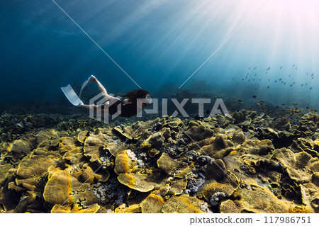 Freediver woman swims over coral reef with sun rays in tropical sea 117986751