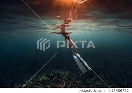 Woman freediver relaxing on surface of ocean after diving. Woman freediving on morning with warm sun light 117986752