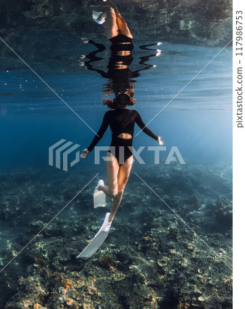 Woman freediver enjoys swimming in blue ocean on the reef. Vertical shot Woman freediver enjoys swimming in blue ocean on the reef. Vertical shot 117986753