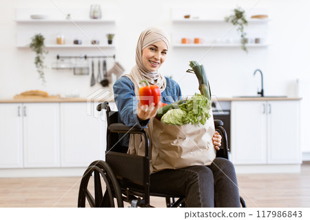 Muslim woman in wheelchair holding vegetables in modern kitchen 117986843