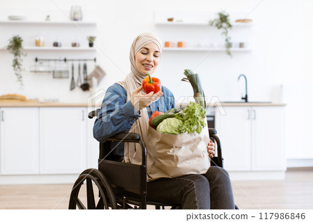Muslim woman in wheelchair with fresh vegetables in kitchen Muslim woman in wheelchair with fresh vegetables in kitchen 117986846