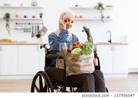 Muslim woman in wheelchair with fresh vegetables in kitchen 117986847