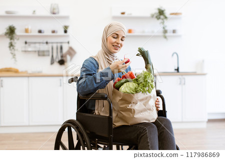 Muslim woman in wheelchair holding paper bag with fresh vegetables Muslim woman in wheelchair holding paper bag with fresh vegetables 117986869