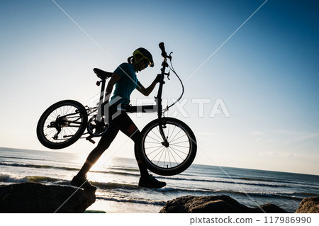 Woman taking a folding bike on sunrise seaside Woman taking a folding bike on sunrise seaside 117986990