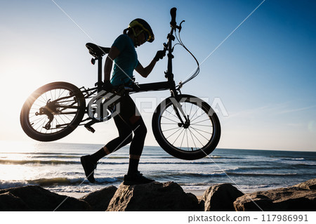 Woman taking a folding bike on sunrise seaside 117986991
