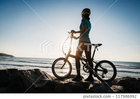 Woman taking a folding bike on sunrise seaside Woman taking a folding bike on sunrise seaside 117986992