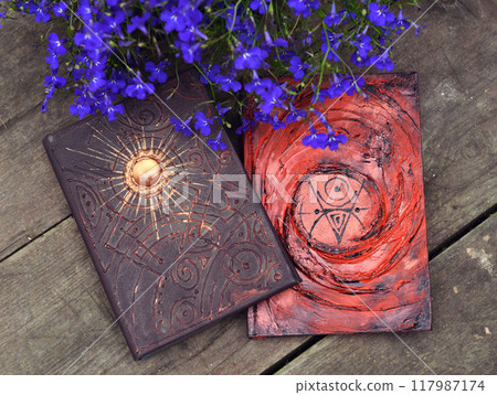 Mystic still life with magic book of spells and flowers on old wooden table. Occult, esoteric, wicca and divination background. Reading and knowledge concept Mystic still life with magic book of spells and flowers on old wooden table. Occult, esoteric, wicca and divination background. Reading and knowledge concept 117987174