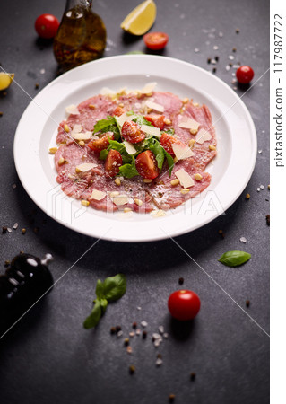 cooking tuna carpaccio - cherry tomato pieces on a plate with raw tuna fillet slices 117987722