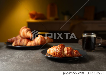 Fresh baked croissants and black coffee on a kitchen table. 117988539