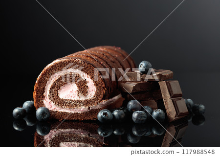 Chocolate roll cake with blueberries and a broken black chocolate bar. 117988548