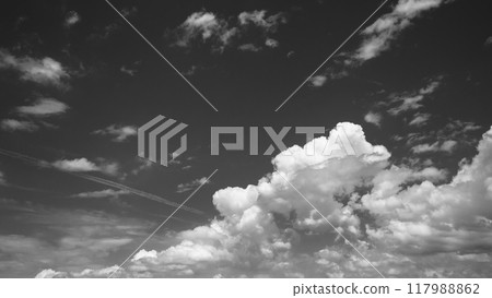 Cumulus clouds and contrails floating in the late summer blue sky, monochrome Cumulus clouds and contrails floating in the late summer blue sky, monochrome 117988862