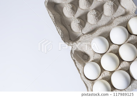 White eggs in a cardboard box on a white background with copy space. White eggs in a cardboard box on a white background with copy space. 117989125