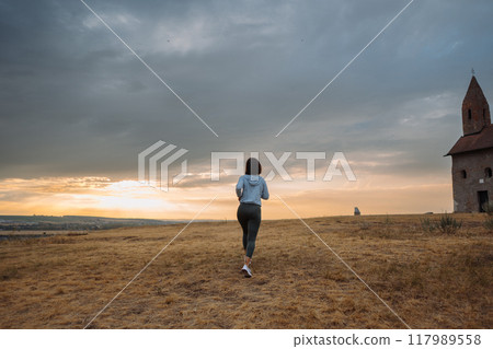 Woman Jogging by Historic Church at Sunset in Scenic Countryside 117989558