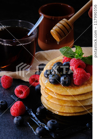 pancakes with berries and honey on dark background 117990356
