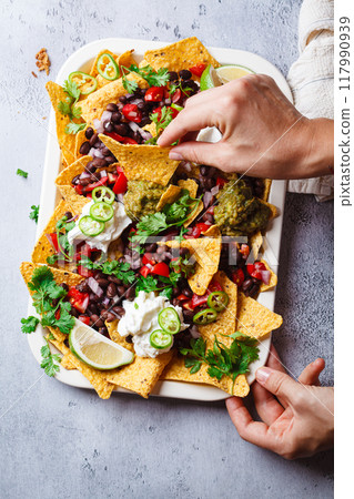 Loaded vegan nachos with guacamole, black beans and salsa for party, top view. 117990939