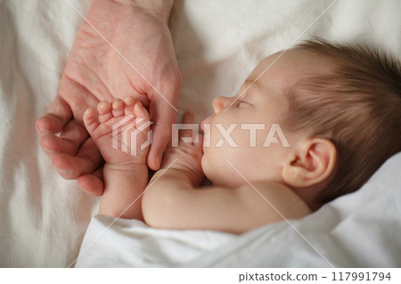 Little Baby's hand into parent hands. Family happiness concept. Sleeping newborn Little Baby's hand into parent hands. Family happiness concept. Sleeping newborn 117991794