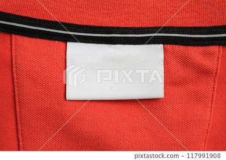 Blank white laundry care clothes label on orange shirt fabric texture background Blank white laundry care clothes label on orange shirt fabric texture background 117991908