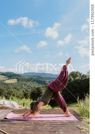 Young woman doing yoga outdoors against hilly landscape 117992008