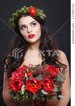 Beautiful young woman with floral head wreath looking up while standing against black background 117992132